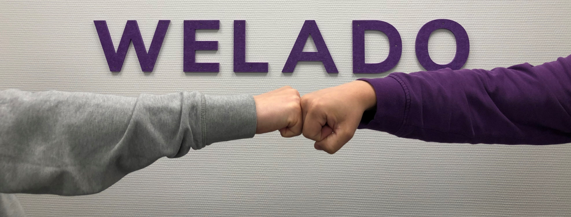 
			    
					
					Kahden ihmisen nyrkit yhdessä Weladon logon edessä.
					
				
			  