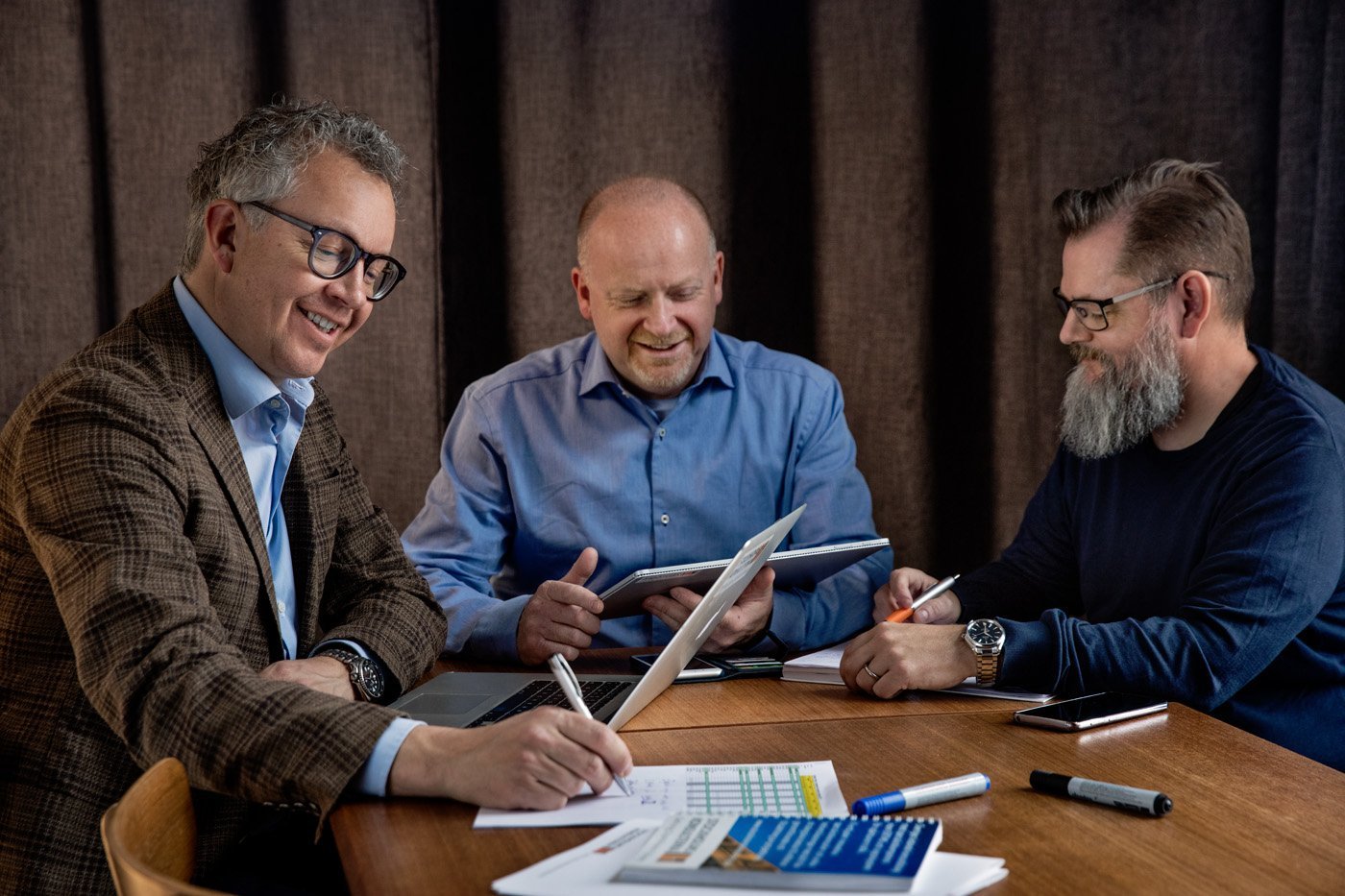 
			    
					
					Kolme miestä tapaamisessa pöydän ääressä iloisena tehden töitä.
					
				
			  